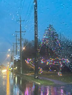 the rain is falling down and there are many lights on the trees in the street