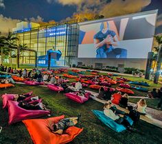 many people are sitting on bean bags in front of a large screen and watching movies