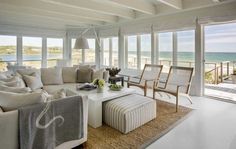 a living room filled with lots of furniture and large windows overlooking the beach in front of it