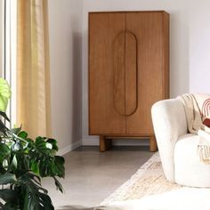 a living room with a white couch and wooden cabinet in the corner next to a potted plant