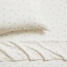 two pillow cases sitting next to each other on a white bed with pink and blue flowers