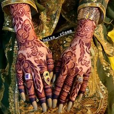 two hands with henna designs on them and gold jewelry around the wrist, both holding onto each other