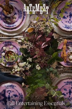 the table is set with purple plates and flowers