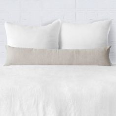 a white bed with two pillows on top of it and a brick wall in the background