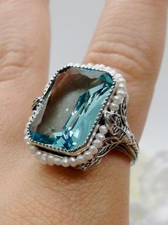 Simulated Aquamarine & Seed Pearl Ring Description  Rectangle Seed Pearl Leaf Design#234 MADE TO ORDER  This is a stunning Victorian reproduction in sterling silver filigree with a simulated aquamarine rectangle stone... The stunning stone is 18mm by 13mm...The ring sits 21mm NS by 19mm EW... The inside of the band is marked 925 for sterling. Notice the beautiful craftsmanship of the silver filigree setting and band. The small natural pearls are 2mm wide... The ring is 9mm off the finger This is Blue Rectangular Jewelry With Accent Stones, Rectangular Sapphire Jewelry For Wedding, Elegant Turquoise Rectangular Stone Jewelry, Elegant Turquoise Jewelry With Rectangular Stone, Blue Aquamarine Jewelry With Rectangular Stone, Rectangular Aquamarine Wedding Jewelry, Blue Rectangular Aquamarine Jewelry, Rectangular Blue Aquamarine Jewelry, Blue Rectangular Jewelry With Gemstone Accents