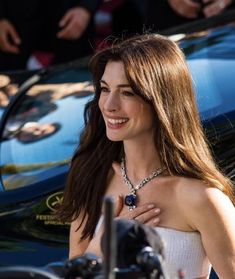 a woman standing next to a blue car with other people around her looking at the camera