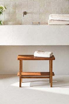 a wooden bench sitting in front of a white bath tub next to a flower vase