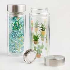 two glass jars with plants in them on a white surface next to a metal strainer