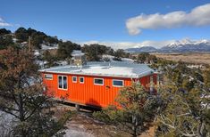 an orange tiny house in the woods with mountains in the background