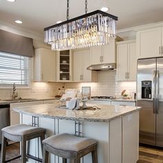 a kitchen island with stools and a chandelier hanging from it's ceiling