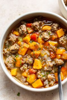 two bowls filled with meat and vegetable soup on top of a white countertop next to a spoon