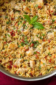 a pan filled with chicken and rice on top of a red cloth next to a spoon