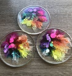 three clear bowls with colorful flowers in them on a table top, one is filled with water and the other has feathers