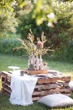 an outdoor table set up with plates and vases on top of wooden pallets