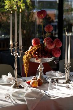 the table is set with candles, fruit and flowers in a silver bowl on it