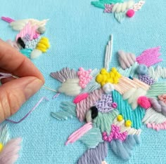 someone is stitching flowers on a piece of blue fabric with needle and thread in the middle