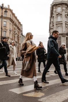 people are crossing the street in front of some tall buildings and one man is wearing a brown coat