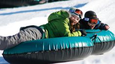 three people riding on an inflatable tube down a snow covered slope