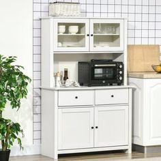 a white cabinet with a microwave on top of it next to a potted plant