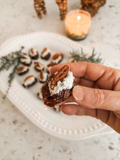 a hand holding a piece of food on top of a white plate next to pine cones