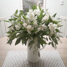 a white vase filled with flowers sitting on top of a table next to a striped place mat