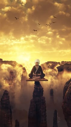 a man sitting on top of a rock formation in the middle of clouds with birds flying overhead