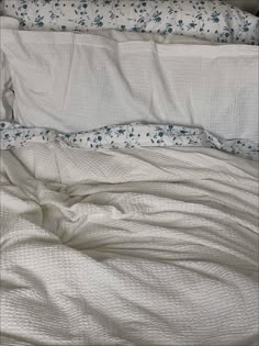 an unmade bed with white sheets and blue flowers