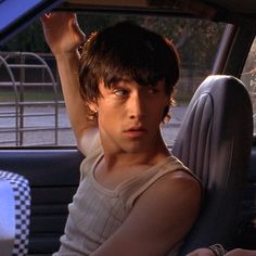 a young man sitting in the driver's seat of a car holding his hand up