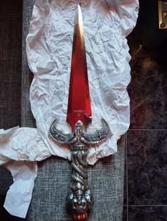 a red knife on top of a white piece of paper next to a metal object