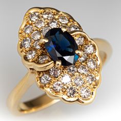 This pretty dinner ring is centered with one (1) oval cut natural sapphire set into a four-prong setting. The sapphire is bordered with twenty-eight (28) bead set round brilliant cut diamonds. The ring measures 18.1mm at the top and rises 8.3mm above the finger, tapering to 2.3mm wide and 1.2mm thick at the base of the shank. It is currently a size 6.5 and is crafted in 14k yellow gold. Art Deco Oval Sapphire Ring With Accent Stones, Art Deco Oval Sapphire Ring With Center Stone, Art Deco Oval Sapphire Ring With Prong Setting, Formal Sapphire Ring With Oval Accent Stones, Elegant Sapphire Oval Cluster Ring, Formal Sapphire Cluster Ring With Rose Cut Diamonds, Elegant Yellow Gold Lab-created Sapphire Ring, Art Deco Sapphire Ring In 14k Gold, Exquisite Oval Sapphire Ring With Diamond Accents