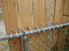 a chain link fence with barbed wire around it and a wooden gate in the background