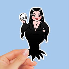 a hand holding up a sticker with a skull in the shape of a woman