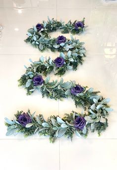 purple flowers and green leaves are arranged in the shape of an e on a white tile floor