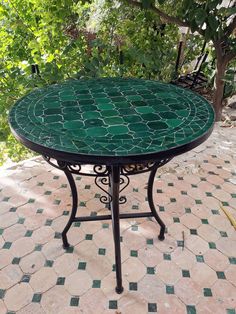 a green table sitting on top of a tiled floor next to a tree and bushes