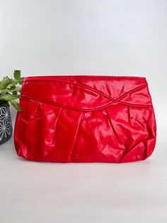 This bag features a red vinyl body with a unique ruffled design. It has two large inner compartments that keep your essentials organized and easily accessible. The detachable strap offers multiple carrying options, making it easy to switch between a clutch and a shoulder bag. Measuring 13 inches by 8 inches. Expected wear for a vintage item with minor surface wear. See pictures for additional description. Thanks for looking! Red Satchel Evening Bag For Party, Red Clutch Evening Bag With Removable Pouch, Red Clutch Evening Bag With Detachable Strap, Red Clutch With Removable Pouch For Party, Red Party Clutch With Removable Pouch, Red Shoulder Bag With Removable Pouch For Party, Red Clutch With Removable Pouch, Red Crossbody Clutch For Party, Red Evening Bag With Zipper Closure