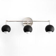 three black balls are hanging from a metal bar on a white wall with two lights