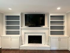 an empty living room with built - in bookshelves and a flat screen tv above the fireplace