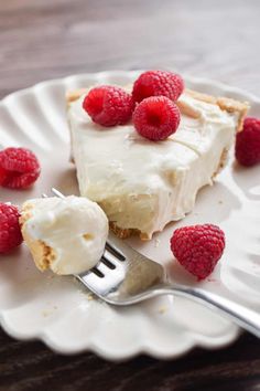 a white plate topped with a slice of pie and raspberries next to a fork