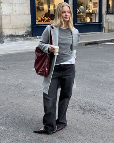 a woman standing in the street with her hand on her hip and holding a purse