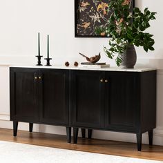 a black cabinet with two candles and a potted plant