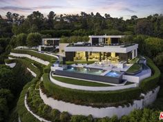 an aerial view of a modern home surrounded by lush green trees and bushes, with a swimming pool in the foreground