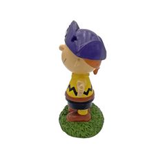 a figurine of a boy with a purple hat and yellow shirt sitting on top of green grass