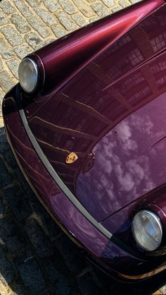 the front end of a purple sports car parked on a brick road with its hood up