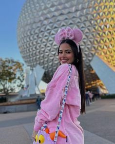 a woman wearing a pink outfit and carrying a purple bag in front of a disney world