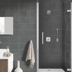 a bathroom with grey tiles and white fixtures, including a shower head, sink, mirror, and towel rack