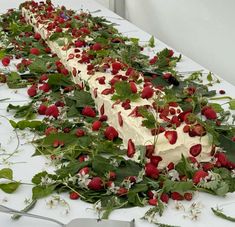 strawberries and flowers are arranged on the table to make a long cake with cream frosting