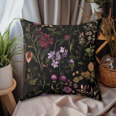 a black pillow with pink and purple flowers on it next to a potted plant