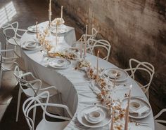 a long table set with white plates and candles for a formal dinner or wedding reception