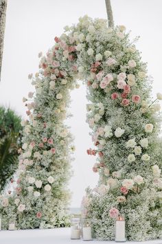 an outdoor ceremony with white and pink flowers on the arch, surrounded by palm trees