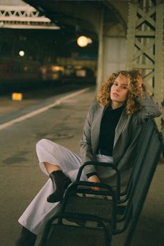 a woman sitting on top of a metal bench next to a train platform at night